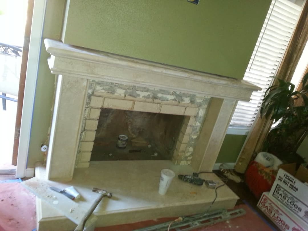 Fireplace under renovation in a green-walled room with tools and materials scattered around.