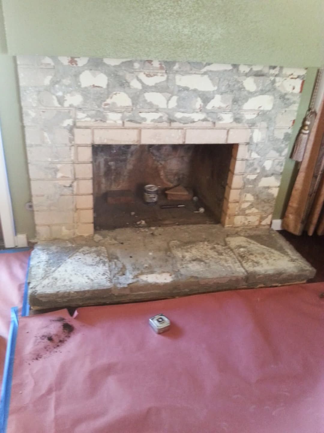 Old brick fireplace with stained stone hearth, surrounded by green walls and floor covering.