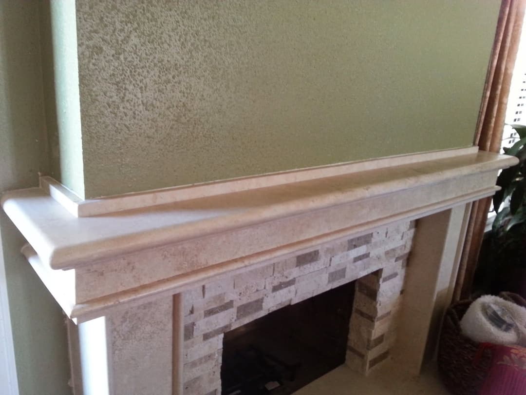 Elegant stone fireplace mantel with a light green wall and textured details.