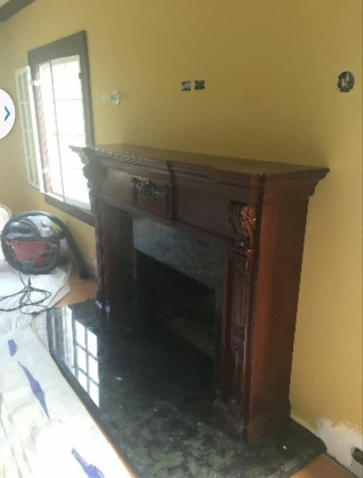 Elegant wooden fireplace mantel against a yellow wall, with marble base and home renovation tools nearby.