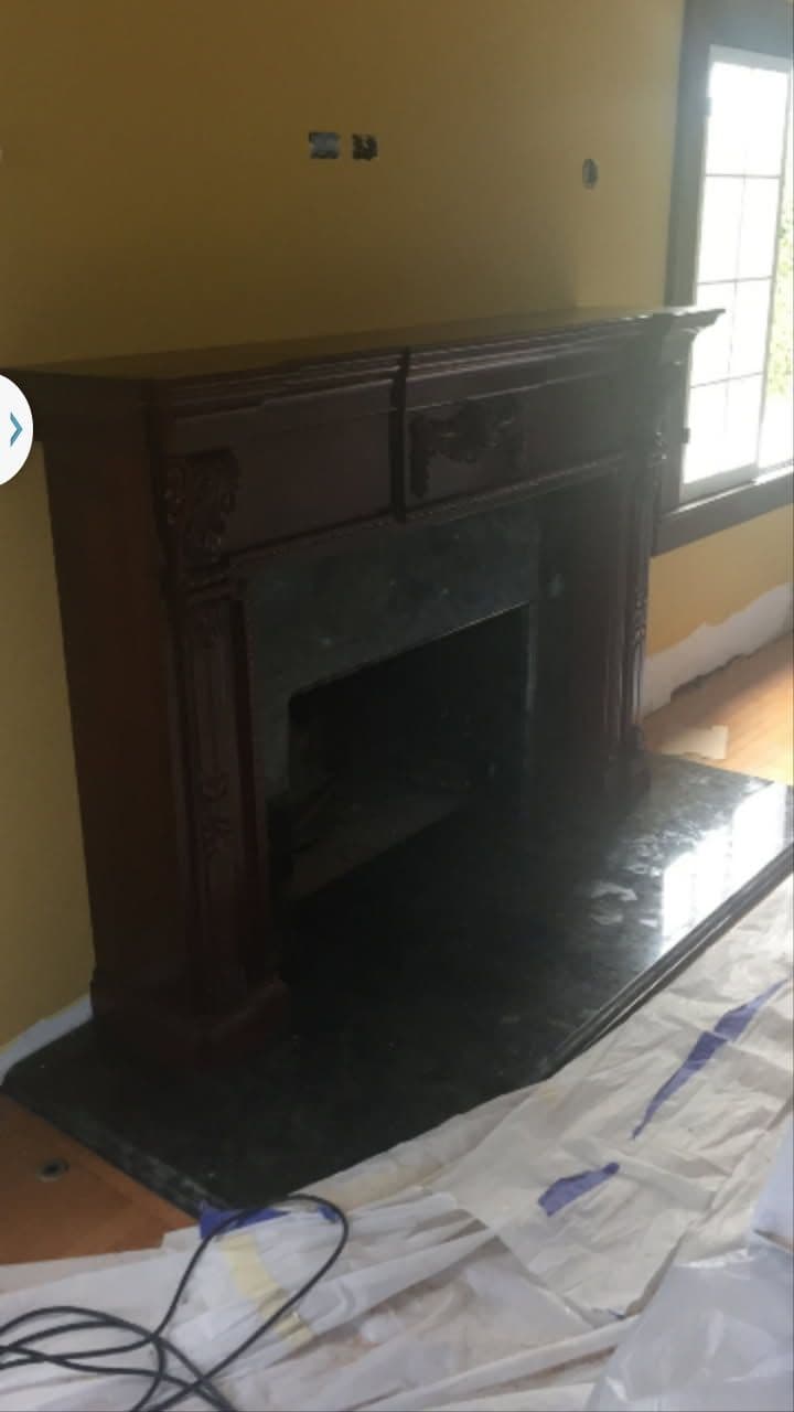 Elegant wooden fireplace mantel with a dark marble hearth against a yellow wall.