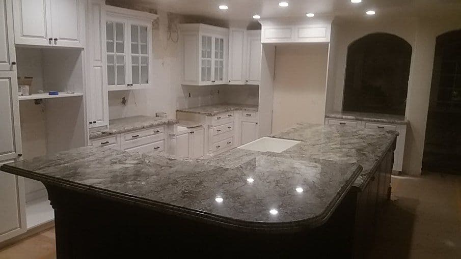 Modern kitchen with granite countertops, white cabinets, and bright lighting.
