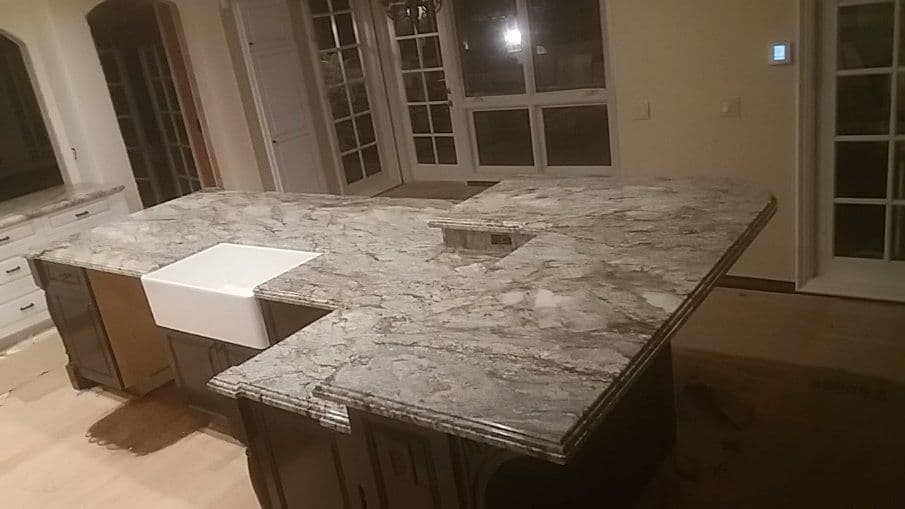 Modern kitchen with a large granite island and a farmhouse sink, featuring natural light and elegant design.