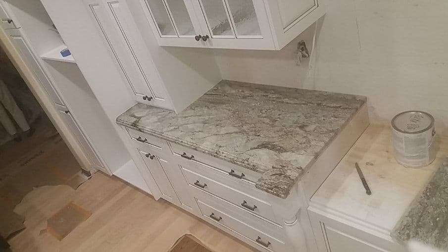 Elegant kitchen countertop featuring gray and white marble with white cabinetry.