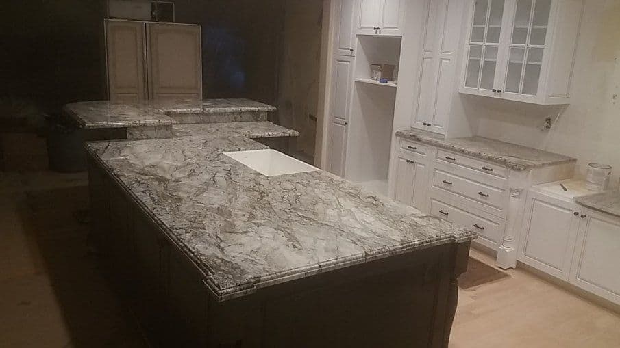 Modern kitchen with gray marble countertops and white cabinetry, showcasing a spacious island.