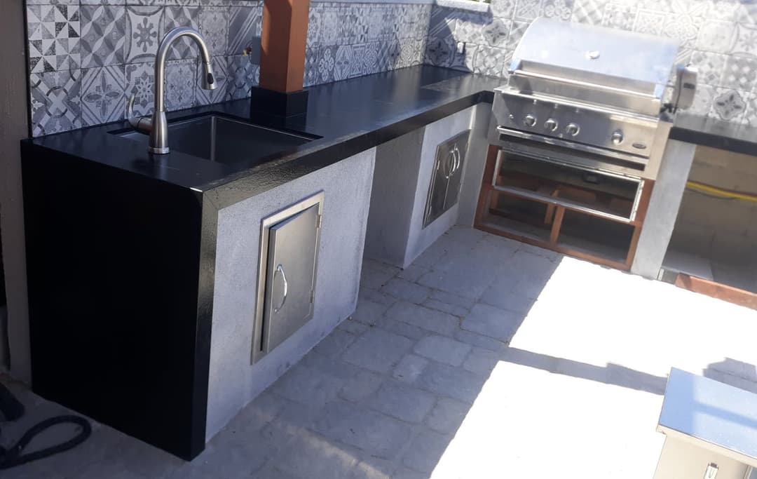 Modern outdoor kitchen featuring a black countertop, sink, and stainless steel grill.