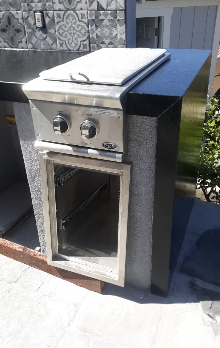 Outdoor kitchen grill station with stainless steel finish and storage space.