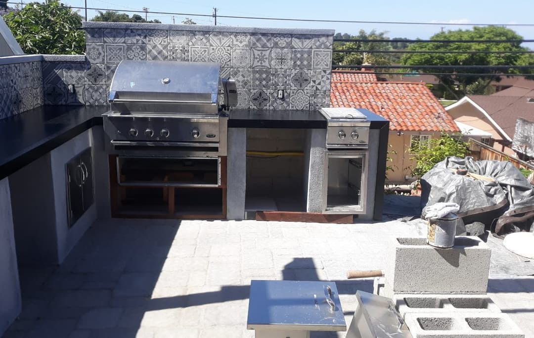 Outdoor kitchen with stainless steel grill, countertop, and stone flooring in a residential setting.