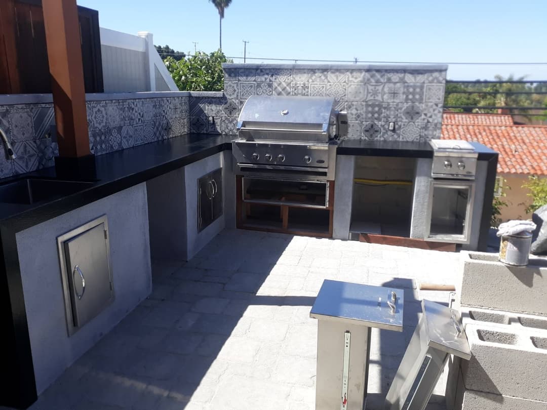 Outdoor kitchen with stainless steel grill, stone countertops, and patterned tile backsplash.