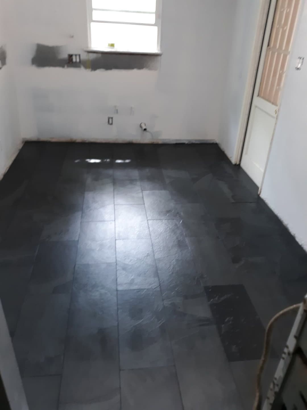 Room with newly installed dark slate flooring and unfinished white walls. Natural light from window.