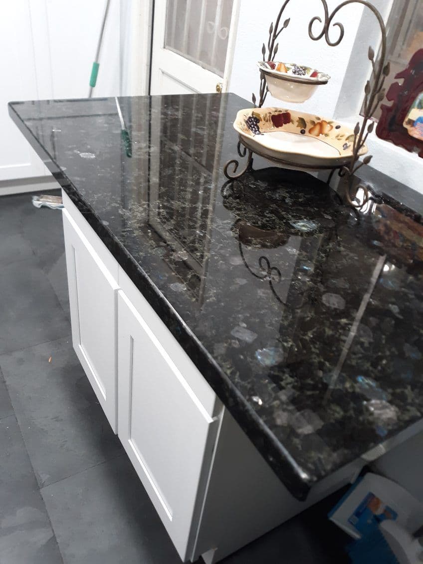 Black granite countertop with white cabinets and decorative plates in a well-lit kitchen.