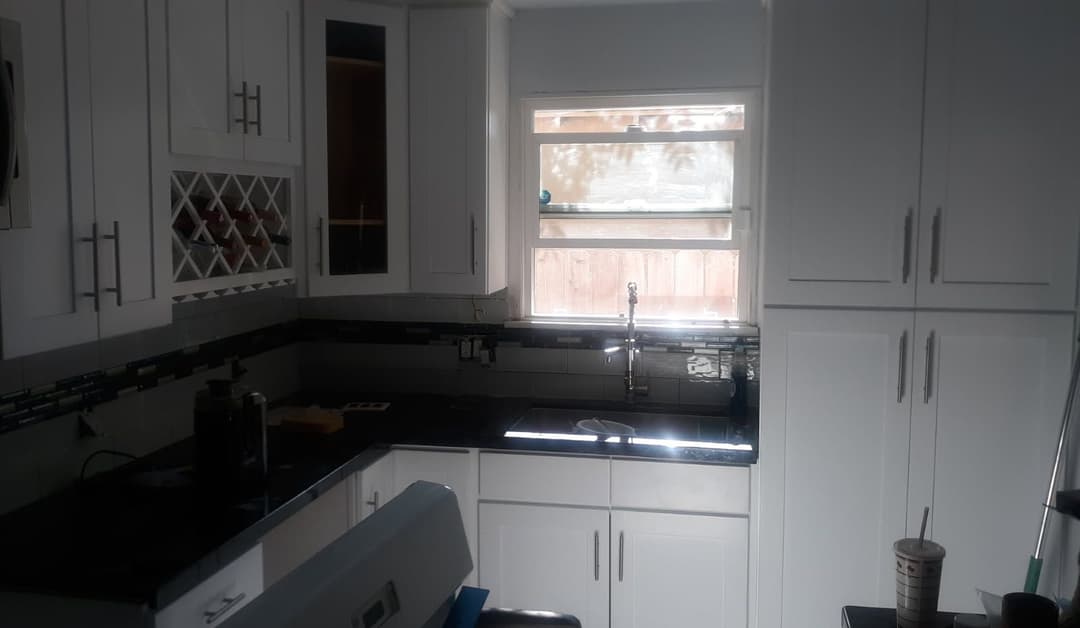 Modern kitchen with white cabinets, black countertops, and natural light from window.