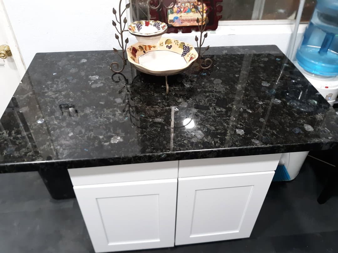Black granite countertop with white cabinets and decorative bowl stand.