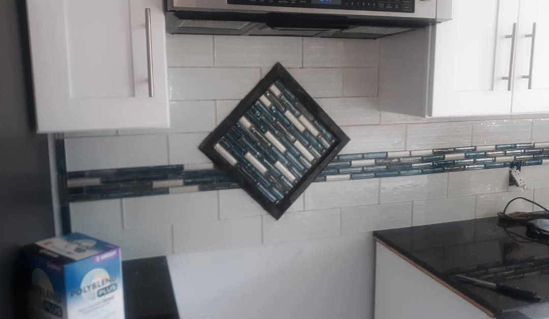 Modern kitchen with white cabinets, black countertop, and stylish diagonal tile backsplash.