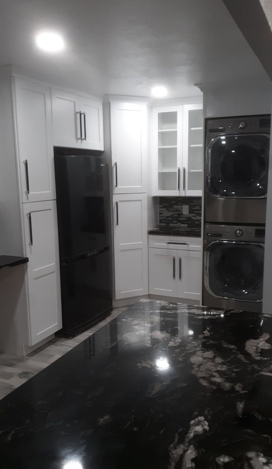 Modern kitchen featuring black appliances, white cabinets, and a striking black marble countertop.
