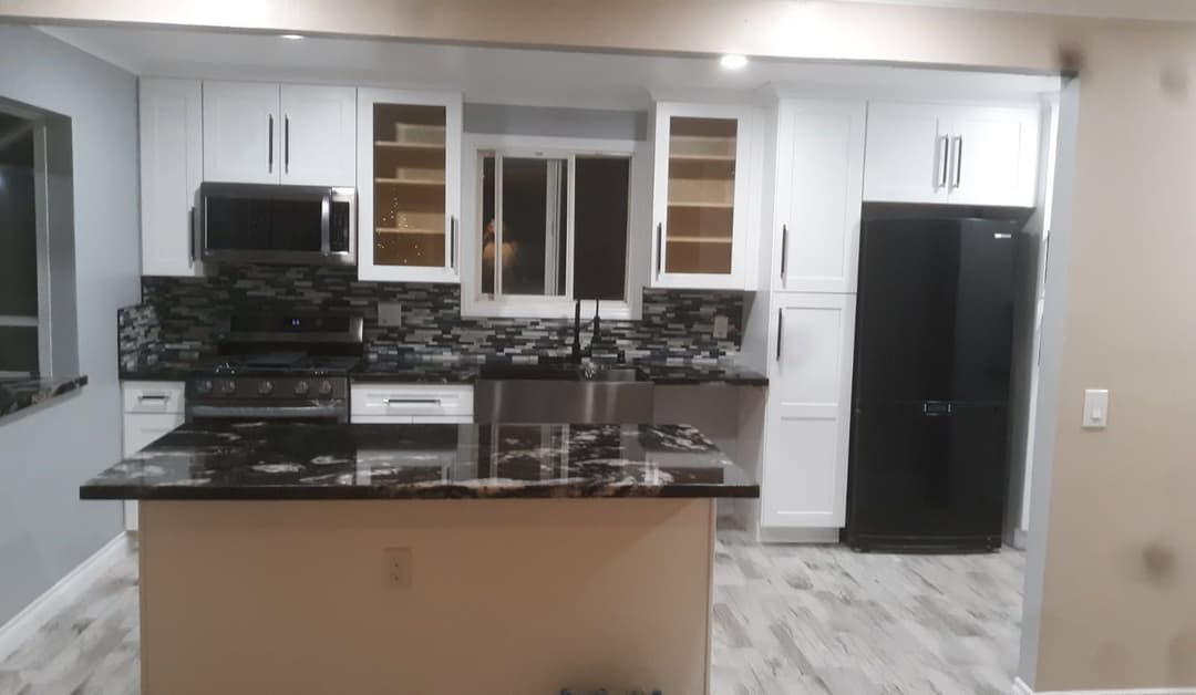 Modern kitchen with black granite countertop, white cabinets, stainless steel appliances, and tile backsplash.