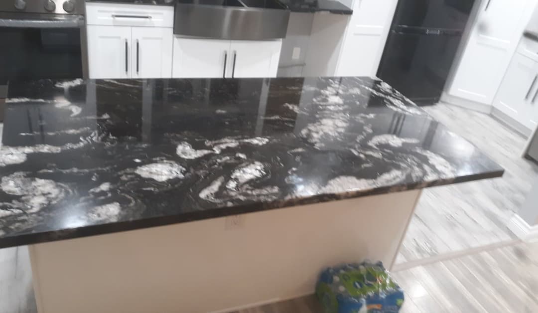 Black marble kitchen countertop with white veining, modern appliances in the background.