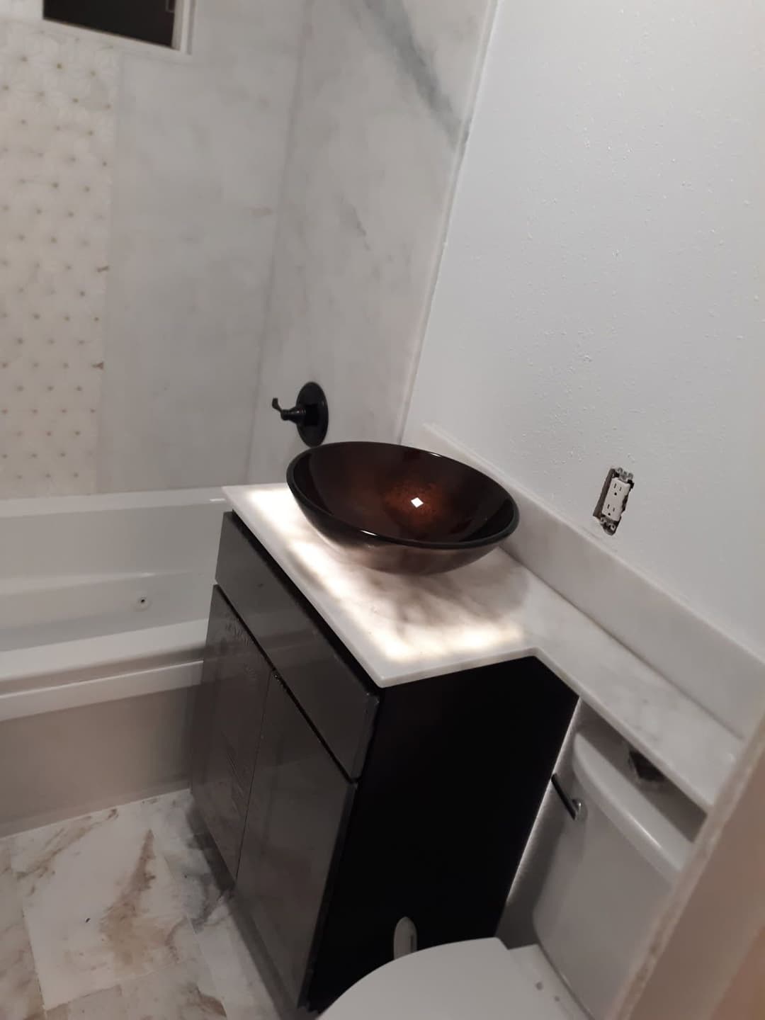 Modern bathroom with marble accents, sleek black vanity, and elegant brown vessel sink.