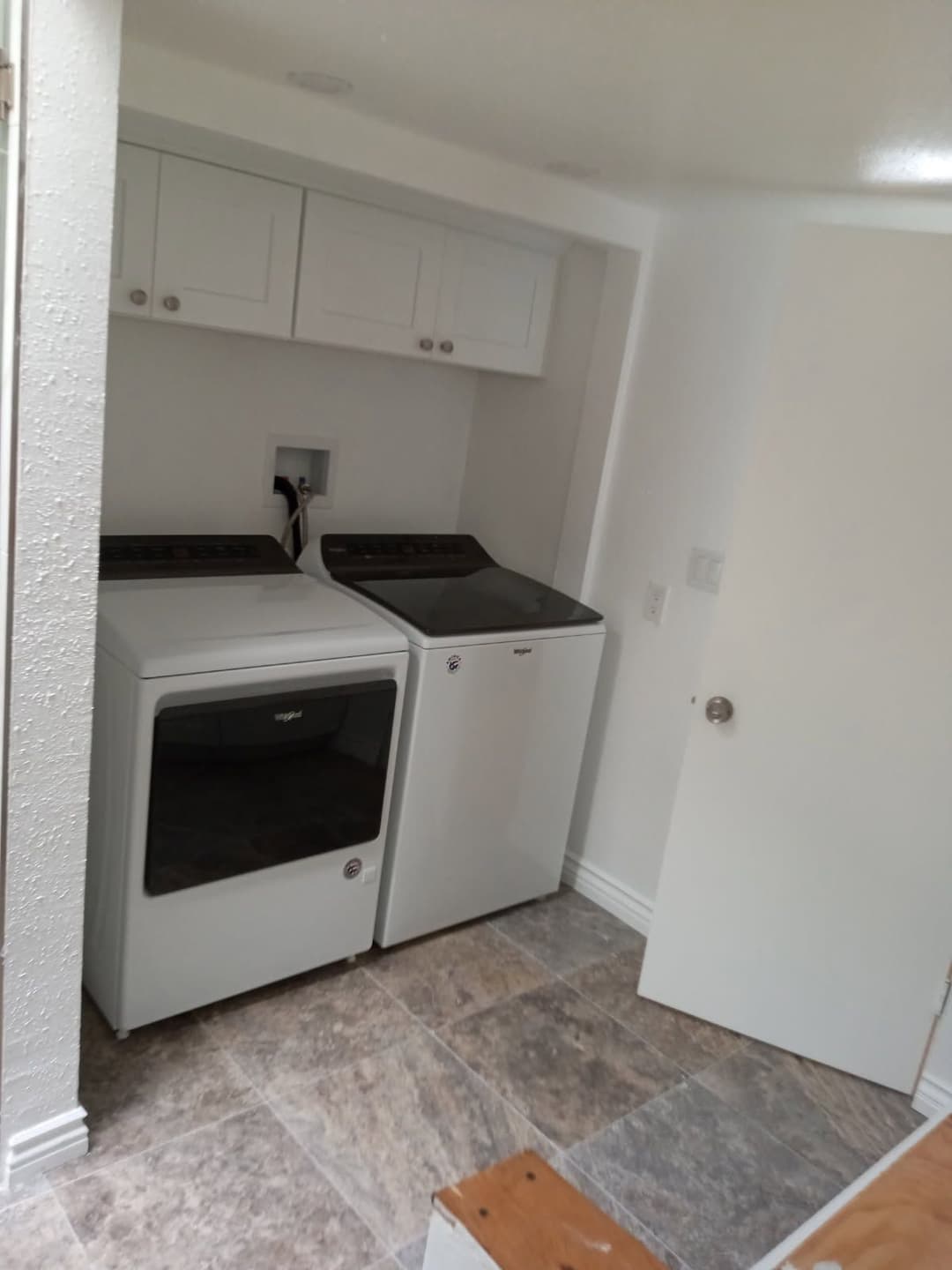 Modern laundry room with white washer and dryer, spacious storage cabinets, and tiled floor.