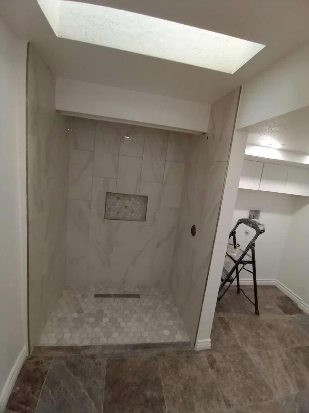 Modern shower renovation featuring marble tiles, a hexagon floor, and a skylight.