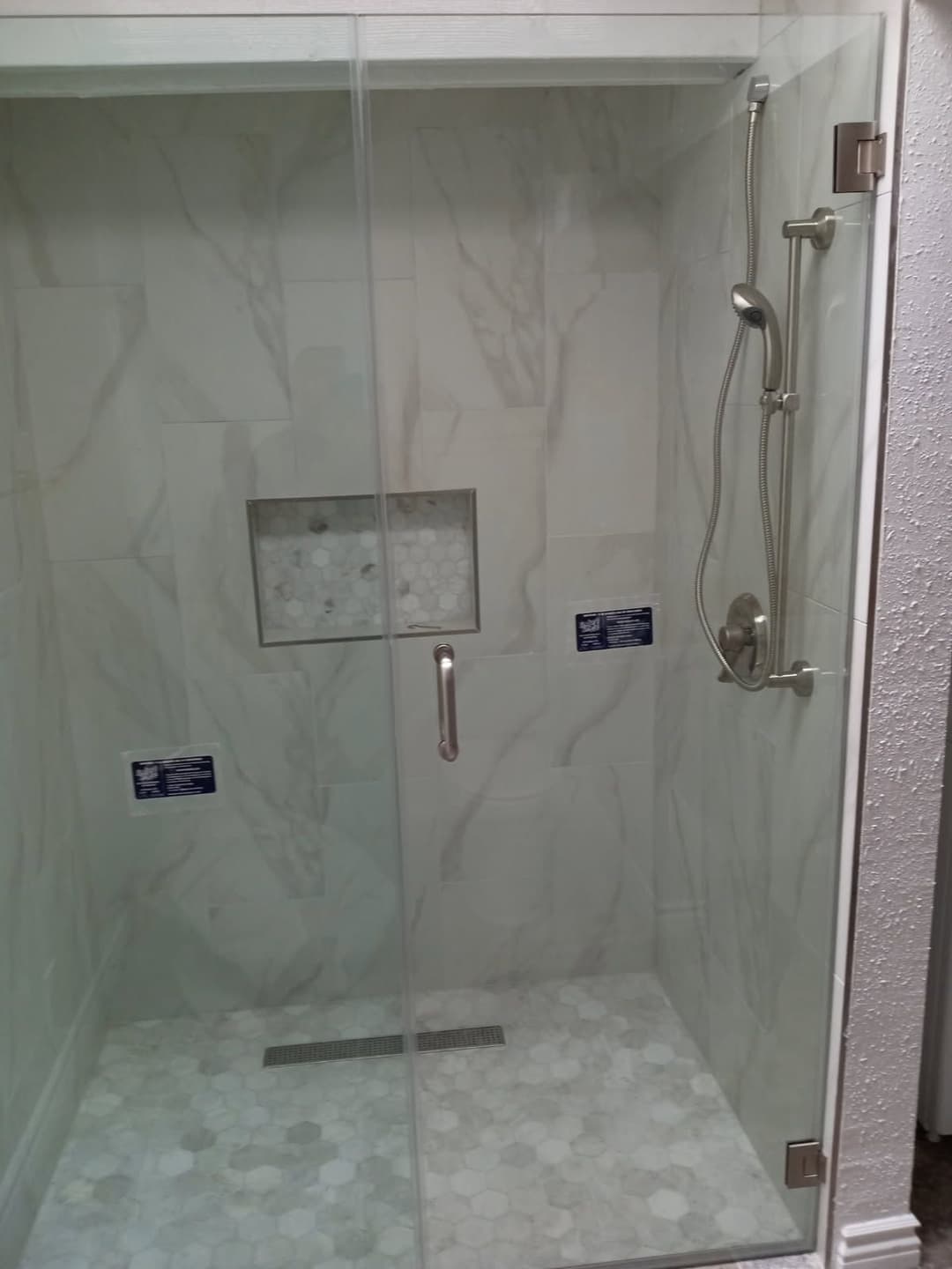 Modern glass shower enclosure with marble tile and hexagonal flooring.