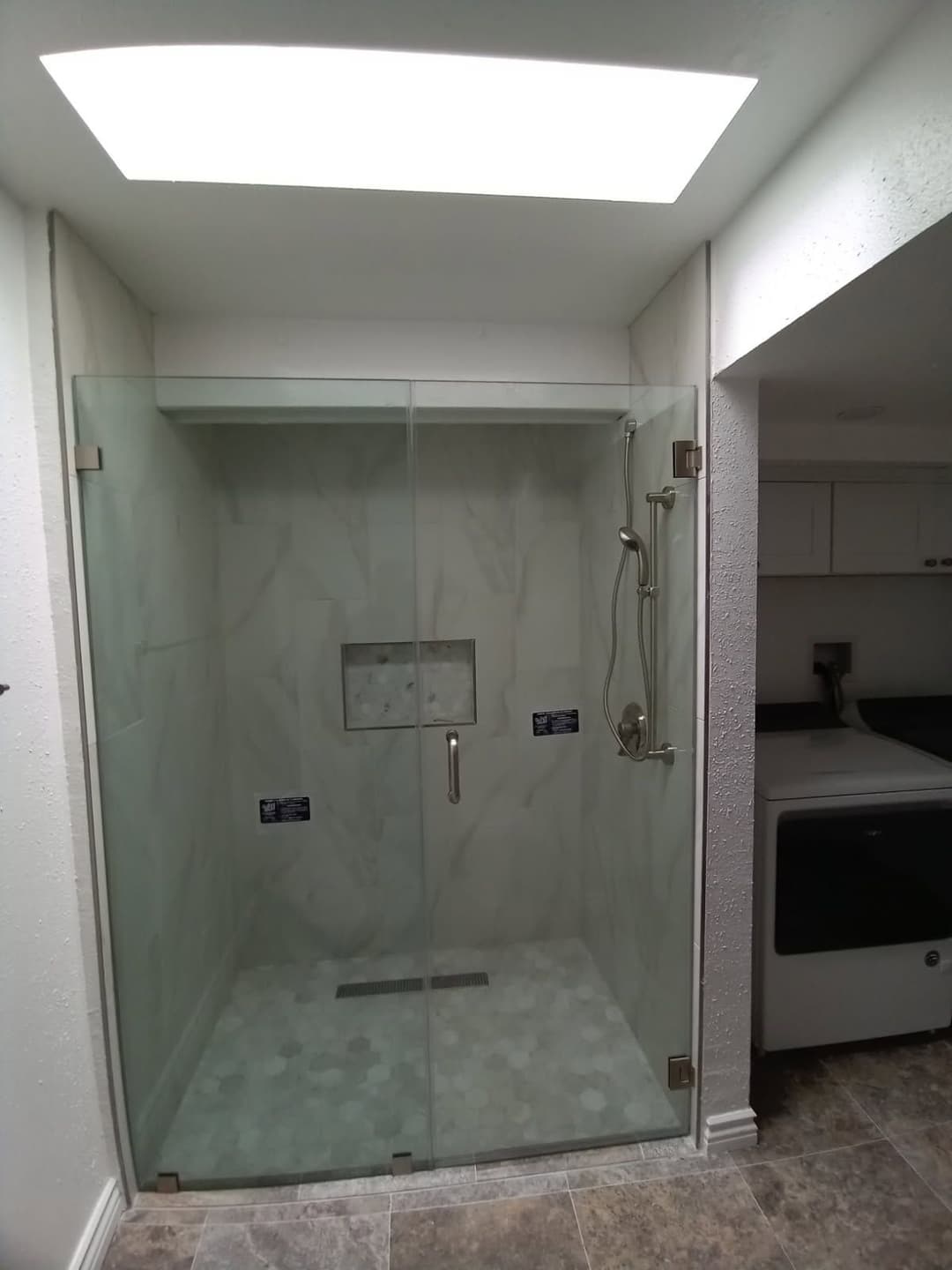 Modern walk-in shower with glass doors, natural stone tiles, and skylight for bright lighting.