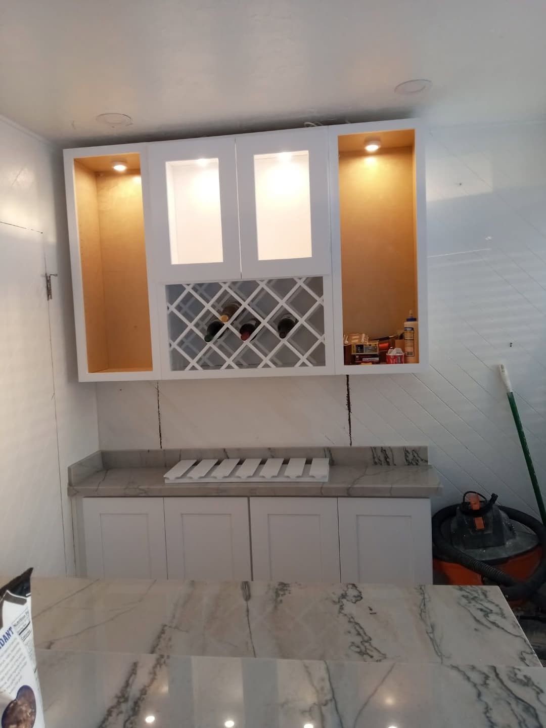 Modern kitchen cabinetry with upper glass doors, wine rack, and marble countertop.