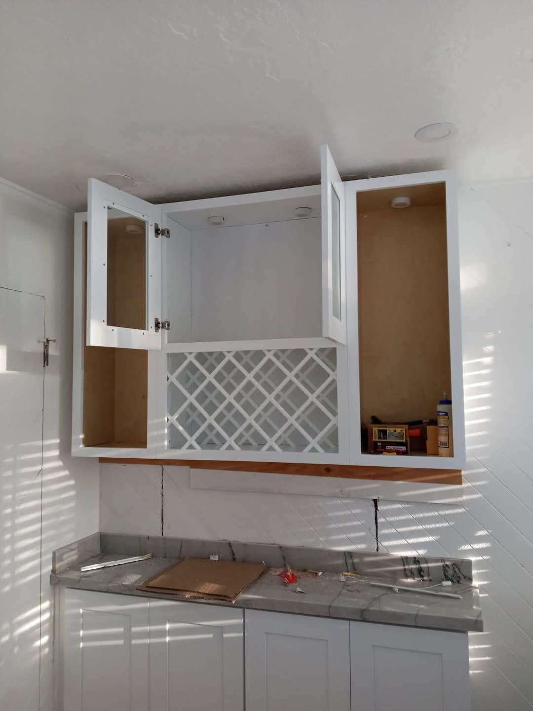 White kitchen cabinet with open doors, displaying empty space and wine rack design.