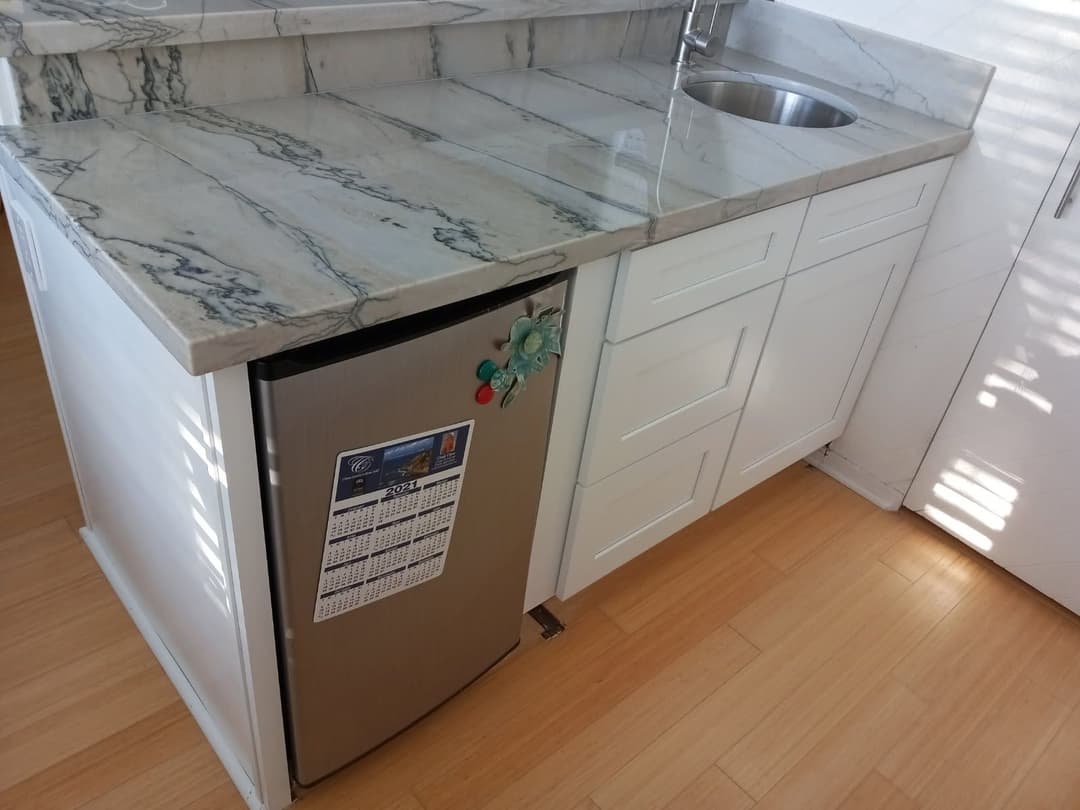 Modern kitchen featuring a stainless steel mini fridge and marble countertop with a sink.