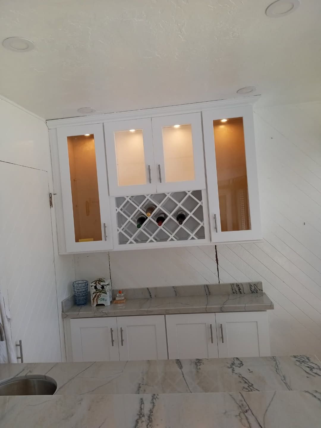 Modern kitchen cabinet with glass doors, wine rack, and polished marble countertop.