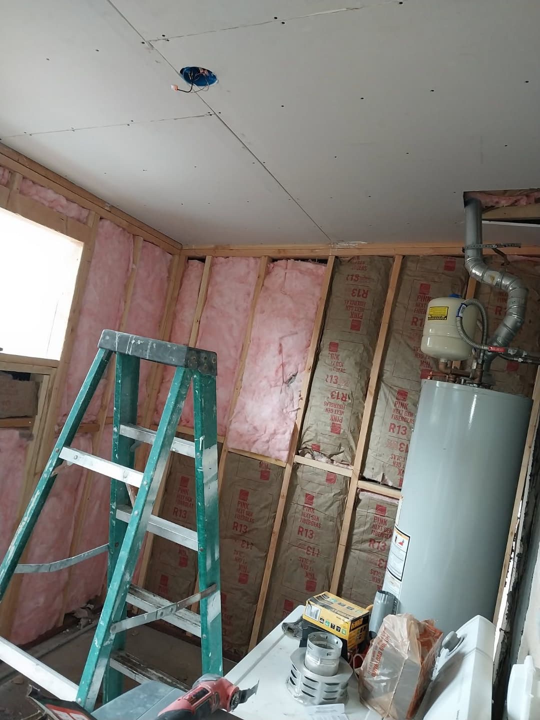 Home renovation project showcasing a room with insulation, a ladder, and a water heater.