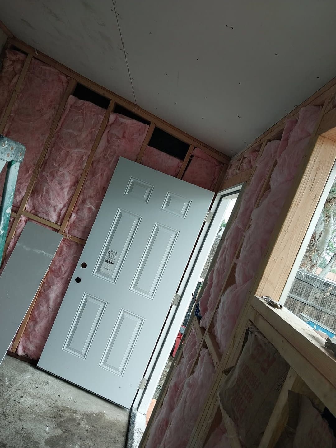 Interior of a room under construction with insulation, featuring a white door and open window.