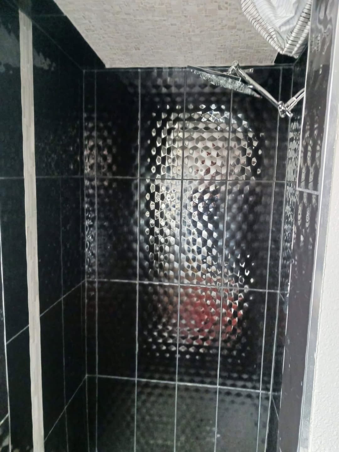 Modern shower with textured black tiles and a sleek chrome showerhead. Stylish bathroom design.