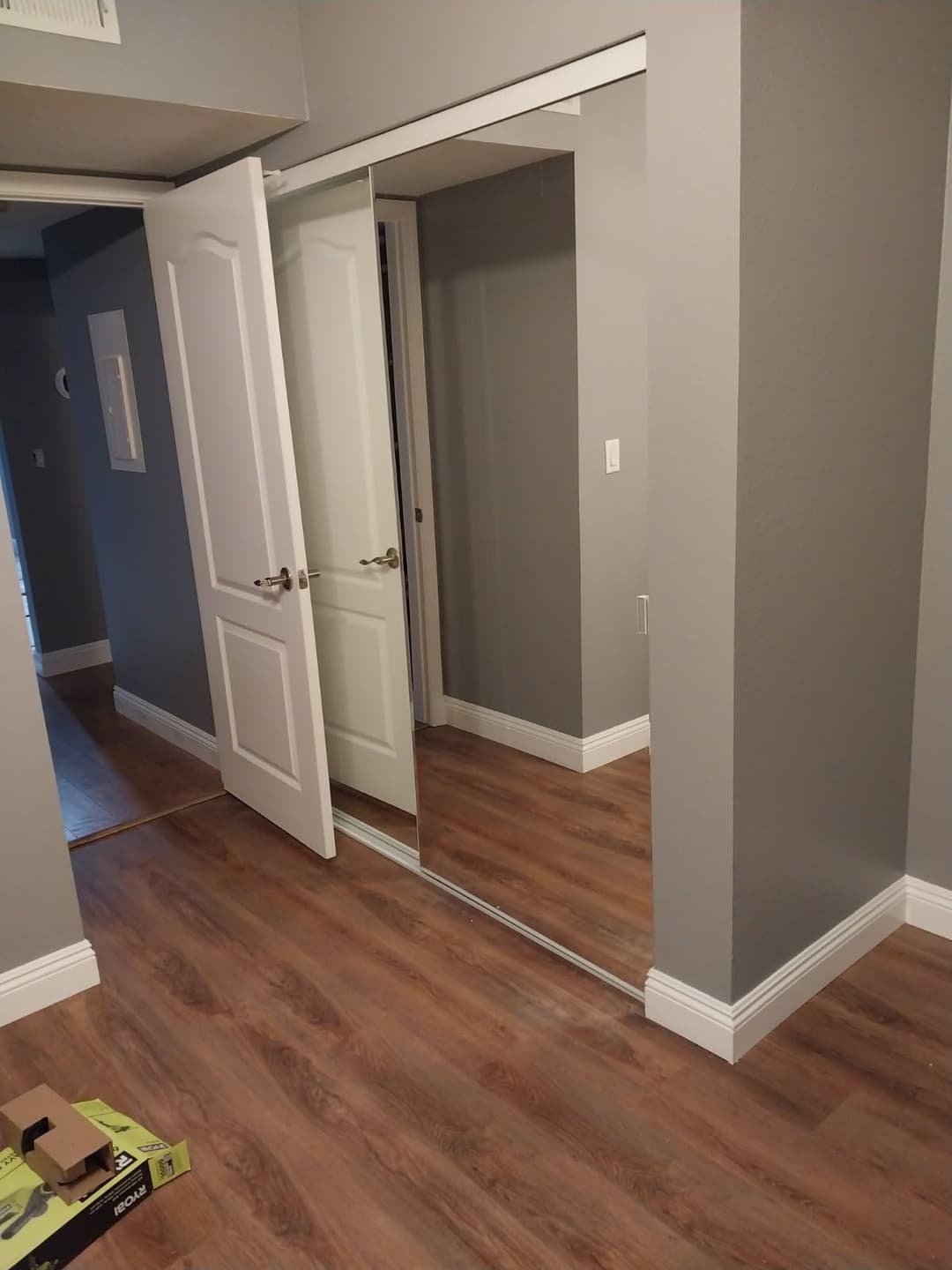 Modern hallway with mirrored closet doors and laminate flooring in a gray painted room.