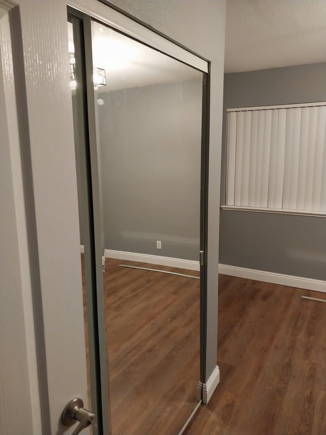 Interior view of a modern room with gray walls, wood flooring, and a sliding mirrored door.