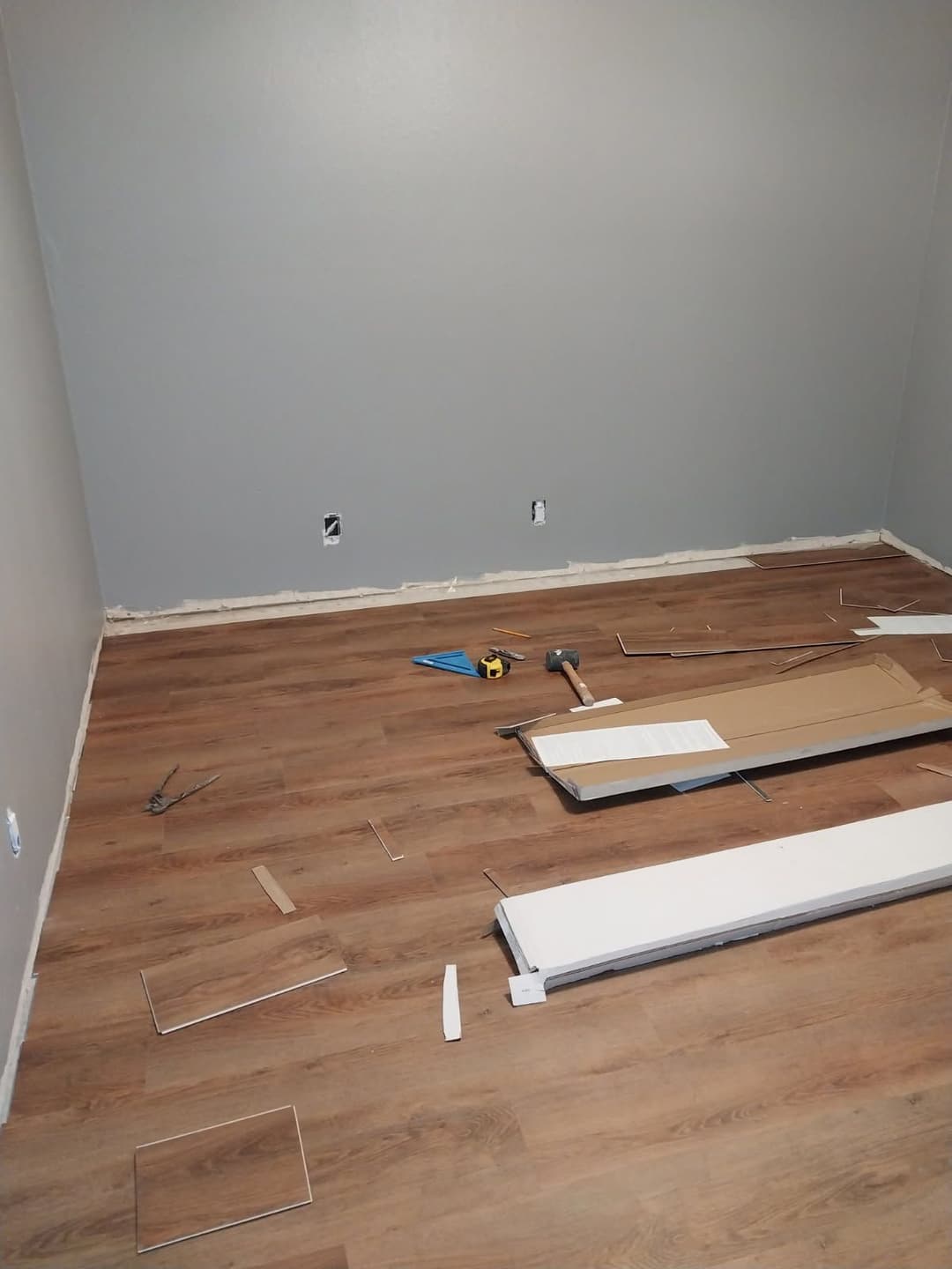 Empty room with wooden flooring under renovation, featuring tools and materials scattered.