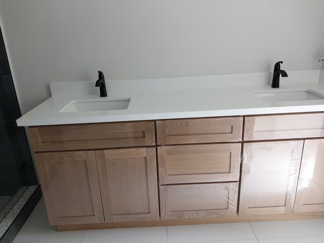 Modern bathroom vanity with light wood cabinetry and black faucets on a white countertop.
