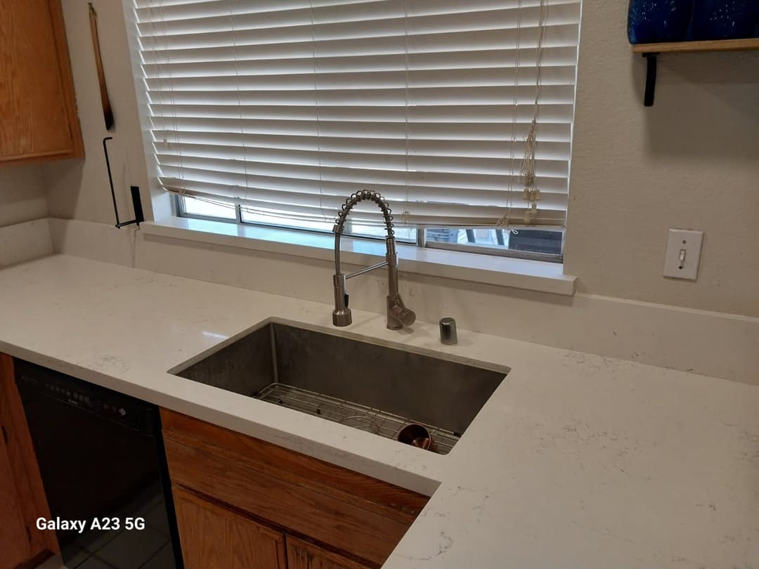 Modern kitchen countertop with a sleek sink and stylish faucet beneath window blinds.