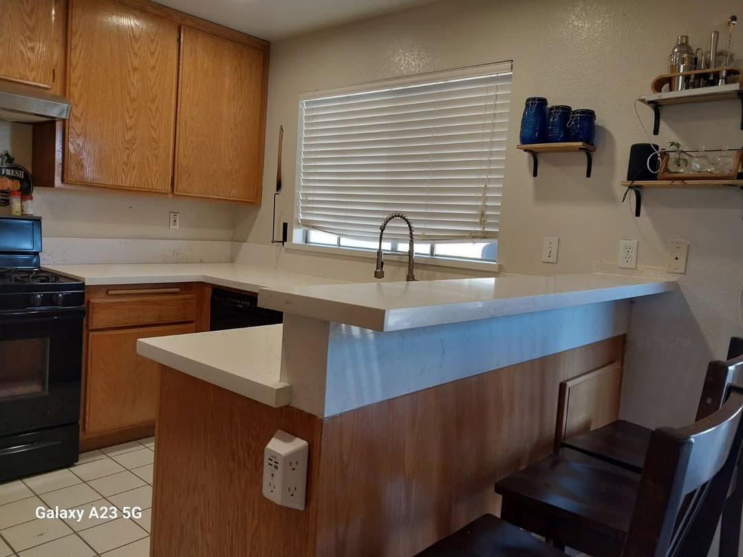 Modern kitchen with wooden cabinets, white countertops, and bar seating near a window.