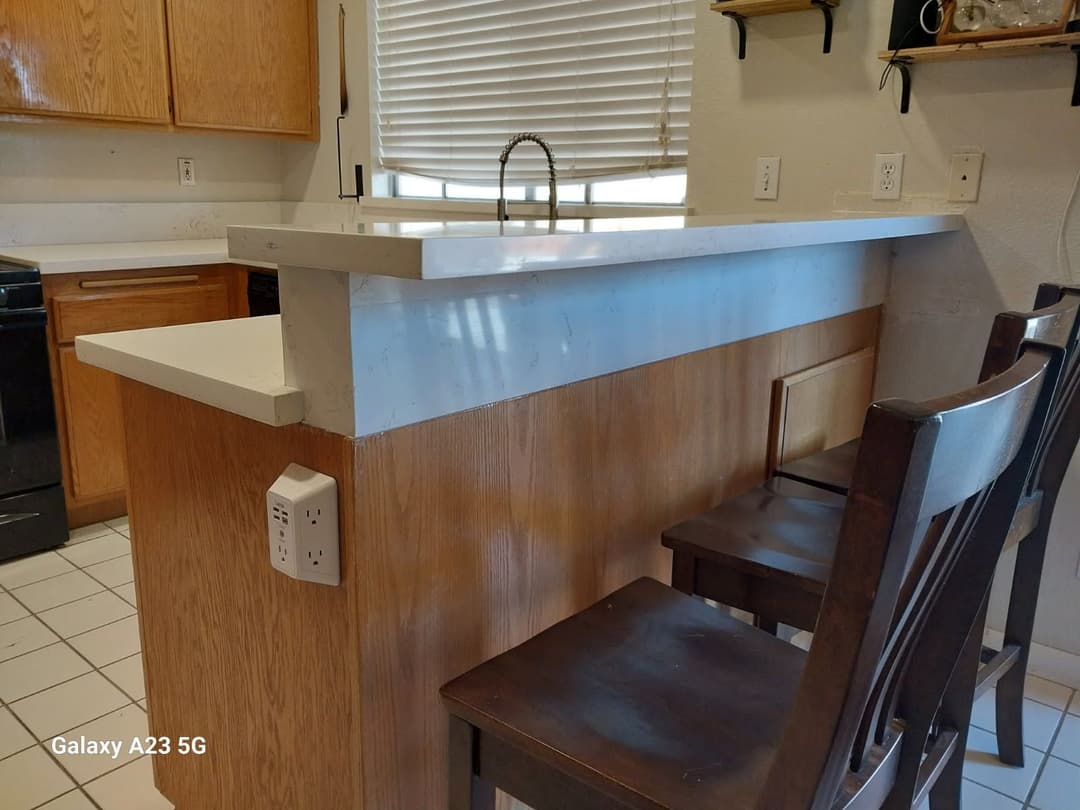 Modern kitchen bar with white countertop and wooden cabinetry, featuring two dark wooden stools.
