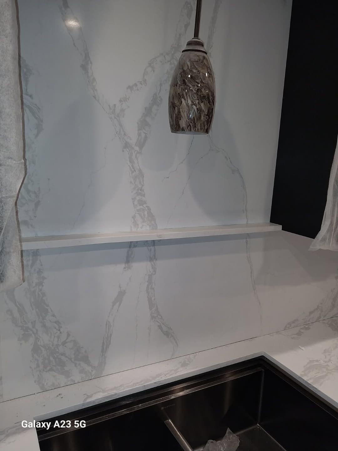 Modern kitchen featuring marble backsplash, sleek sink, and stylish pendant lamp.