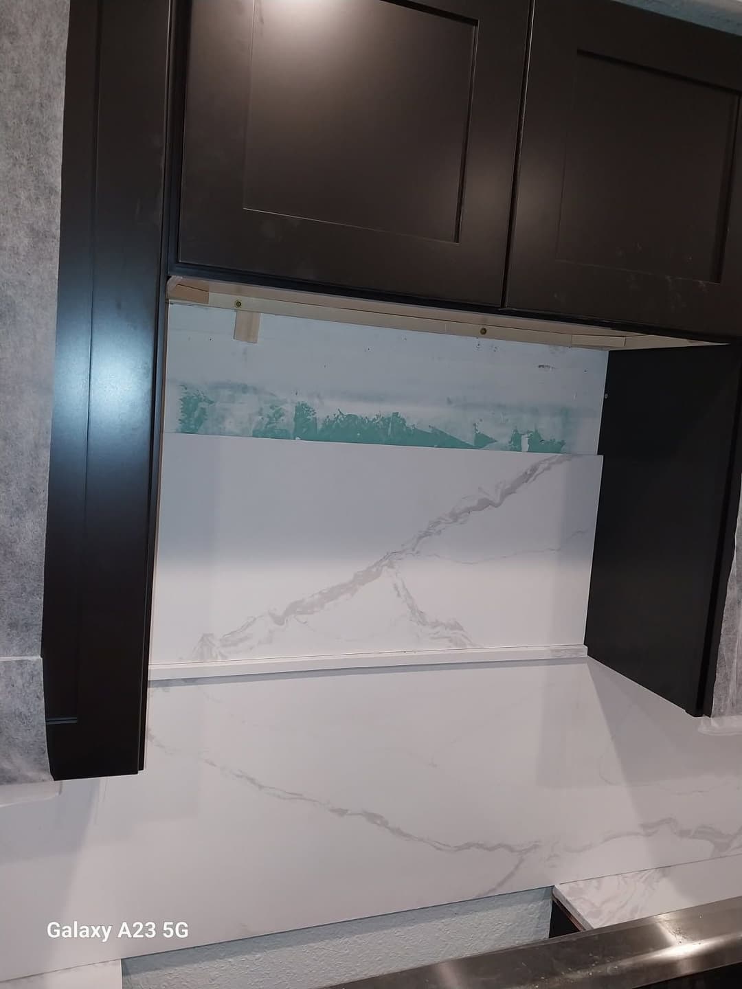 Modern kitchen design featuring dark cabinets and a marble backsplash under construction.