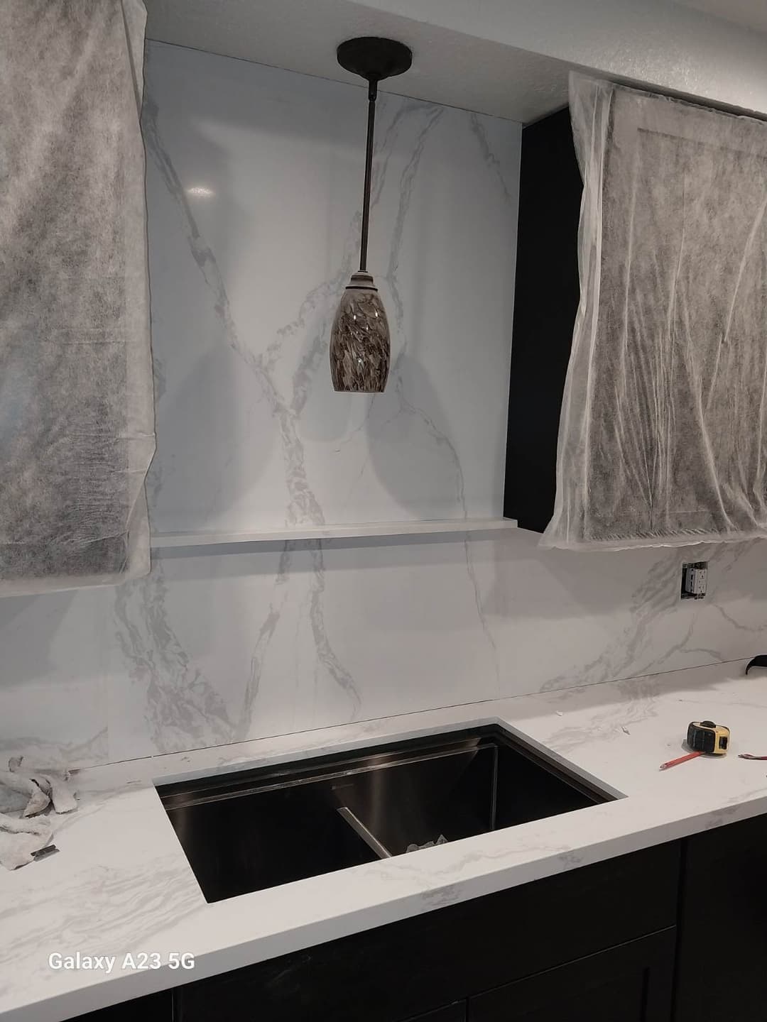 Modern kitchen sink area featuring marble countertops and a stylish pendant light.