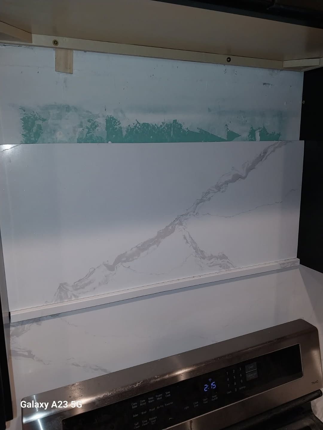 Kitchen backsplash installation in progress, featuring white marble design above a stainless steel oven.