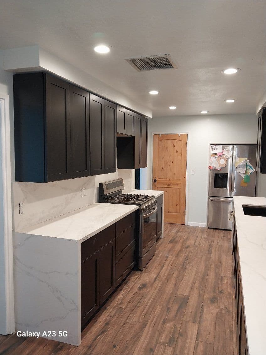 Modern kitchen with dark cabinets, marble countertops, stainless steel appliances, and wood flooring.