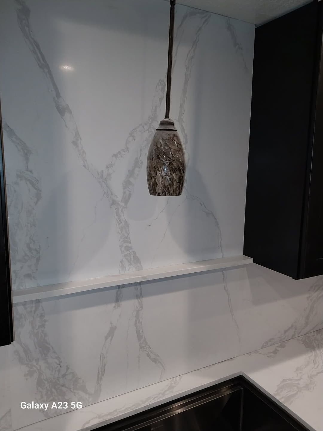 Modern kitchen with white marble backsplash, sleek black cabinets, and stylish pendant light.